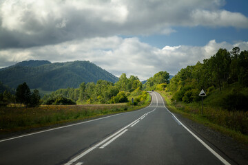 Long road. Highway among white clouds in a blue sky. summer landscape green trees and grass