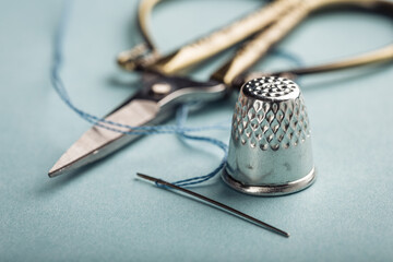 Vintage silver metal thimble and needle, scissors on blue background