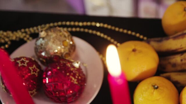 Decorated Christmas table with food. Bananas, oranges, burning candles and Christmas toys and decorations