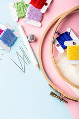 Overhead shot of embroidery set fot cross stitching. White fabric, embroidery hoop, colorful threads, scissors and needls. On pink blue background. Hobbies concept with copy space.