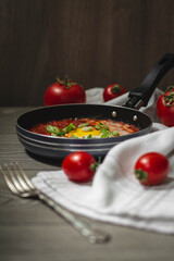 Shakshuka traditional middle eastern dish with tomatoes and eggs in a small pan garnished with scallions and chilli. Tomatoes in the background, dark and moody concept