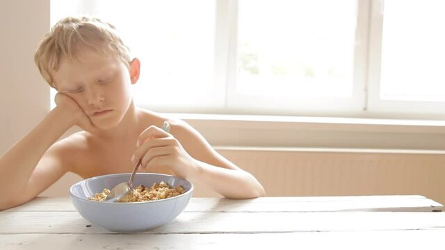 Sleepy boy muddling spoon in his morning cereal before going to school