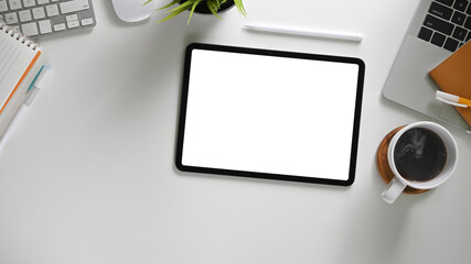 The top view image of white workspace is surrounding by a white blank screen tablet and various...