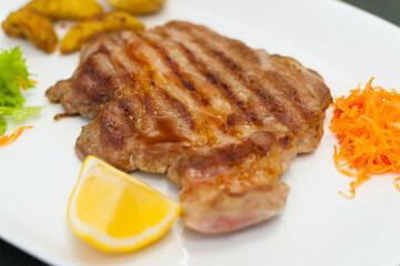 Juicy and delicious grilled meat steak with lemon, carrots, lettuce and potatoes.