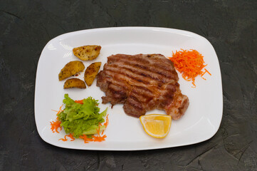 Grilled meat steak with lemon, carrots, lettuce and potatoes. Juicy and very tasty dish of Italian cuisine
