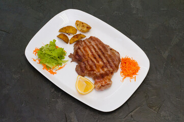 Grilled beef or veal meat steak with lemon, carrots, lettuce and potatoes. Juicy and very tasty dish of Italian cuisine