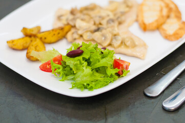 Stewed mushrooms with fish fillet, salad, fried potatoes and croutons, close-up. Tasty traditional italian food