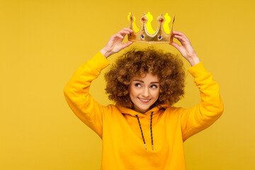 I am queen! Portrait of happy curly-haired hipster woman putting crown on head and smiling, concept...