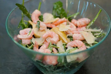 Salad with shrimp, arugula and cheese in glass bowl or plate, dark background, close-up, top view