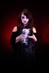 Portrait of a pretty witch with bloody eyes, holding a smoking chalice in her hands