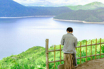 Back view of male tourist enjoy with beautiful scenery view of nature with a large reservoir above the Srinagarind Dam at Rai Ya Yam view point in Si Sawat District, Kanchanaburi Thailand.