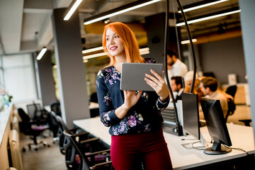 Young businesswoman working on digital tablet while in the background team working in the modern office