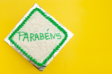 Birthday cake decorated with green icing and grated coconut. Isolated on yellow background. Top view. Copy space. Translation of the word PARABÉNS in English: CONGRATULATIONS.