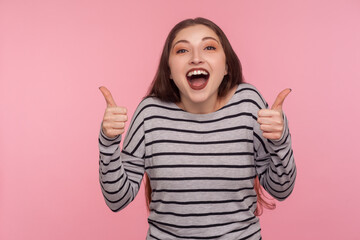 Excellent job, I like it! Portrait of overjoyed excited woman in striped sweatshirt doing thumbs up and shouting in happiness, satisfied with awesome result, successful project. studio shot isolated