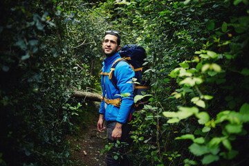 Naklejka na ściany i meble Young hiker with backpack walk in tropical jungle while enjoying wild nature landscape, traveler standing on forest trail against green plants with copy space area for your text message or information