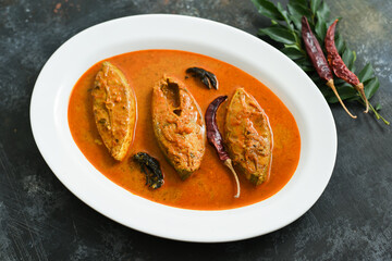 Top view of traditional Goan Pomfret or King fish curry Goa India on dark or black background. Hot and spicy homemade Kerala fish curry yellow curry made using coconut milk , gambooge, turmeric. 