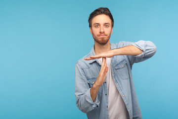 Please, need pause! Portrait of man in worker denim shirt showing time out, refusing and doing enough limit gesture, asking to stop, warning of deadline. studio shot isolated on blue background