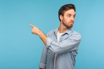 Get out! Portrait of irritated young businessman in casual denim shirt pointing away, scolding for bad result and showing exit, ordering to leave. indoor studio shot isolated on blue background