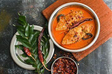 Top view of traditional Goan Pomfret or King fish curry Goa India on dark or black background. Hot and spicy homemade Kerala fish curry yellow curry made using coconut milk , gambooge, turmeric.  - obrazy, fototapety, plakaty