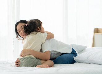 portrait picture of asian mother with smiling face hugs young daughter in bedroom. family relationship and together concept