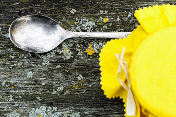 Silver spoon and  glass jar with yellow napkin on the gray vintage wooden background
