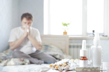 A sick guy is sitting at home on a sofa with a handkerchief and is taking medicine. Selective focus