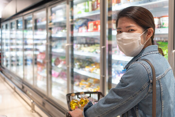 Fototapeta na wymiar young asian woman wearing mask and keeping social distancing while shopping food in supermarket. new normal, covid-10 and coronavirus concept