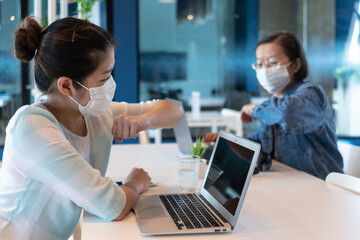 Fototapeta na wymiar two asian woman are wearing face mask and making safe greeting by bumping elbow to say hi during covid-19 or coronavirus outbreak to prevent infection. social distancing and new normal concept
