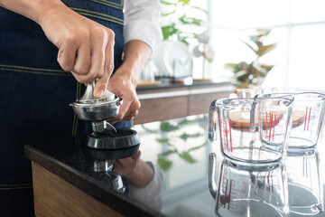 young asian man using coffee grinder machine to gride coffee beans in the cafe. barista concept