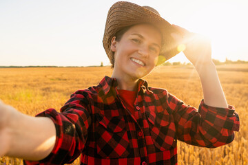 Woman farmer in cowboy hat makes selfie on the background of a wheat field. © scharfsinn86