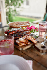 Dinner table with meat grill, roast vegetables, sauces and lemonade, appetizers variety serving on party outdoor table..