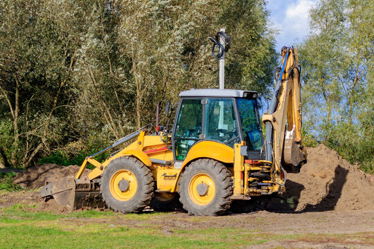 Parked large yellow multifunctional wheel tractor on the glade against green trees in sunny day
