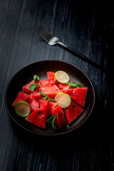 watermelon slices mixed with mint leaves and lemon slices in a black ceramic plate