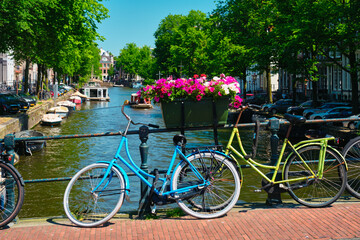 Fototapeta na wymiar Typical Amsterdam view - Amsterdam canal with boats and parked bicycles on a bridge with flowers. Amsterdam, Netherlands
