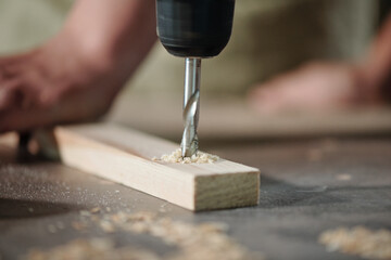 Close-up of unrecognizable carpenter drilling wooden plank to make holes at workplace - obrazy, fototapety, plakaty
