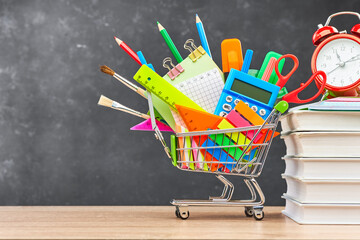 Various office supplies for school in a cart, textbooks and an alarm clock, on a wooden table...