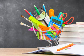 Various office supplies for school in a cart, textbooks and an open notebook, on a wooden table...