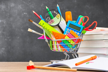 Various office supplies for school in a cart, textbooks and an open notebook, on a wooden table...