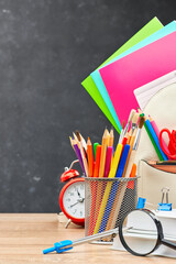 A school bag with colored notebooks, a stand with writing materials,and an alarm clock on a wooden...