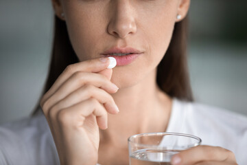 Close up of anxious young woman feel unwell take painkiller antibiotic medicine or pill at home,...