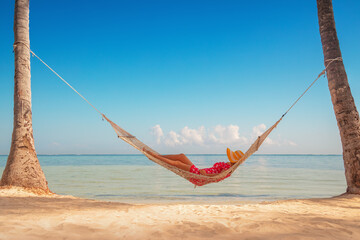 Young girl resting in a hammock under tall palm trees, tropical beach - obrazy, fototapety, plakaty