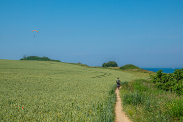  cyclist rides along a very narrow sand path and a paraglider flies on the horizon
