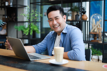 Young Asian Man in blue shirt working with laptop in coffee shop cafe smile and happy face - 360899240