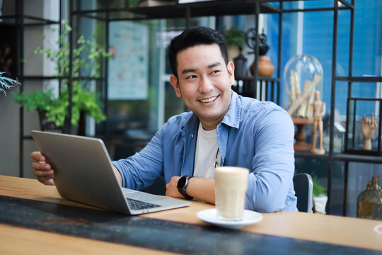 Young Asian Man in blue shirt working with laptop in coffee shop cafe smile and happy face
