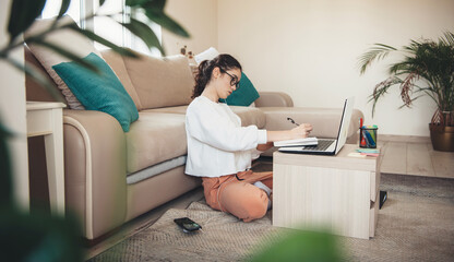 Side view photo of a concentrated caucasian woman with curly hair and eyeglasses writing something...