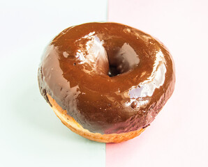 One chocolate donut on a light blue and pink background, top view