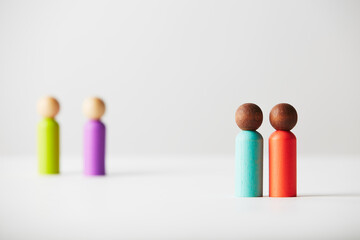 Wooden figures concept. Brown colour skin couple in foreground and white caucasian out of focus couple in the background. Different race couples, genders or age unknown.