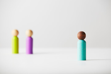 Wooden figures concept. Brown colour skin person standing in front with focus on him and a light skin colour couple of people standing in the back, out of focus. Untold age or gender. Racial concept