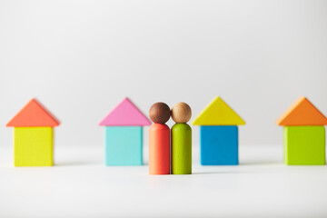 Wooden figurines concept. Two wooden figures people standing in front of a line of block houses, mixed skin colour. Realty market of Residential Development. Kids toys