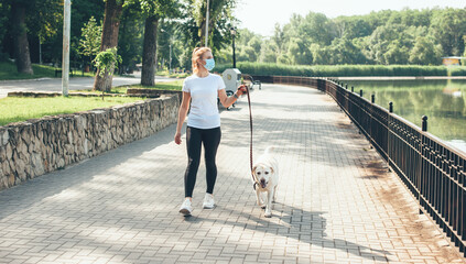 Full sized photo of a caucasian woman with blonde hair and medical mask on face walking with her golden dog